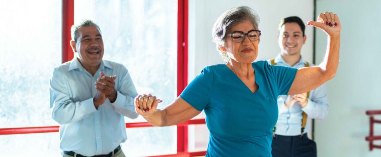 Foto de una señora Latina mayor que tiene mayor riesgo de contraer COVID-19 bailando.